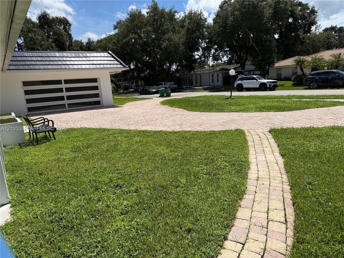 Paved driveway leading to a modern garage door with frosted glass panels, featuring a distinct dark-tiled roof