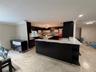 Open-concept kitchen featuring an island with white countertops, dark wood-finish cabinetry, recessed lighting, and tile flooring throughout