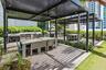 Outdoor kitchen featuring stainless steel appliances, dual metal pergolas, wood-finish decking, and built-in stone-finish counters