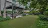 Outdoor terrace featuring a synthetic turf putting green, dual metal-framed pergolas, a built-in outdoor kitchen, and mature privacy hedges