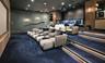 Media room featuring tiered flooring, recessed stair lighting, integrated wooden cabinetry, a projector, and wall-mounted sconce lighting