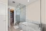 Stone-surround soaking tub with deck-mounted faucet, glass-enclosed shower, wood-finish flooring, and walk-in closet with built-in cabinetry