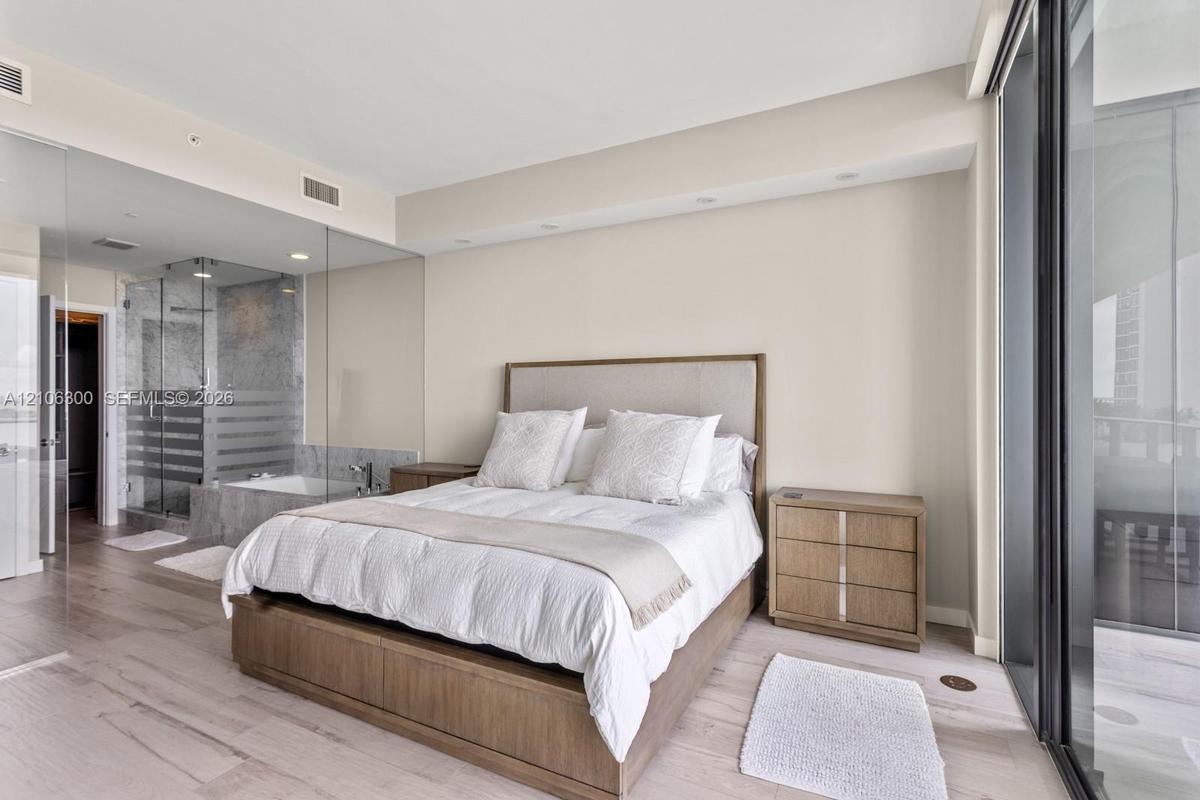 Neutral-toned interior featuring wood-finish flooring, full-height glass partitions, a glass-enclosed shower, and expansive sliding glass doors