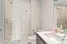 Glass-enclosed shower with tiled surround, vanity featuring an integrated sink, quartz-composite countertop, and wall-mounted mirror