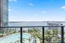 Balcony featuring a dark metal railing, overlooking a large swimming pool, landscaped grounds with mature palm trees, and coastal water