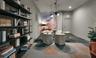 Floor-to-ceiling built-in black metal shelving unit, geometric patterned modular carpeting, decorative marble-finish accent wall, and multi-pendant mo
