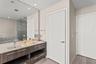 Double vanity featuring a light-toned countertop with integrated dual sinks, wood-finish cabinetry with linear hardware, full-width wall mirror, and r