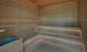 Sauna featuring horizontal wood-slat wall paneling, multi-level tiered wood benches, integrated recessed lighting, and a metal heating unit enclosure