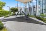 Outdoor recreation area featuring a play structure with a slide, rubberized surfacing, overhead shade canopy, perimeter landscaping, and vertical ligh