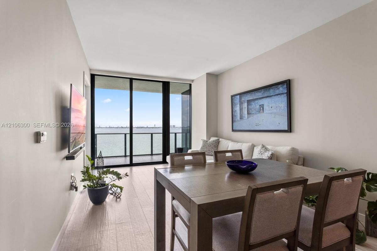 Neutral wall tones, wood-finish flooring, floor-to-ceiling glass sliding doors, and a private balcony featuring a metal railing