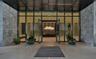 Expansive glass-paneled entrance framed by oversized textured stone cladding, polished stone flooring, and a sleek metal ceiling canopy