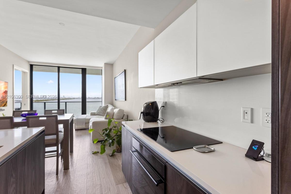 Modern kitchen featuring flat-panel cabinetry, light-toned countertops, a glass-ceramic cooktop, and wood-finish flooring with floor-to-ceiling window