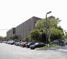 Four-story masonry exterior featuring vertical glass paneling, paved surface parking lot, and mature perimeter landscaping