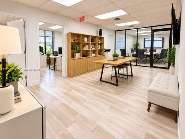 Open-concept office space featuring light wood-finish flooring, built-in floor-to-ceiling wooden shelving, glass-enclosed partitioned office space, an