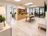Open-concept office space featuring light wood-finish flooring, built-in floor-to-ceiling wooden shelving, glass-enclosed partitioned office space, an