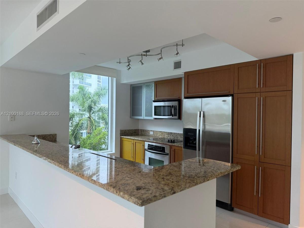 Kitchen featuring stone countertops, breakfast bar, built-in cabinetry with glass-panel upper doors, stainless steel appliances, and track lighting
