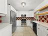 Kitchen featuring white cabinetry, solid-surface countertops, decorative tile backsplash, stainless steel appliances, and floating wooden shelving