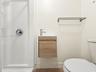 Floating wood-finish vanity with a white countertop and single-handle faucet, integrated shower stall with chrome fixtures, and a wall-mounted metal t