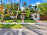 Single-story exterior featuring a clay tile roof, stucco finish, paved walkway, and mature landscaping