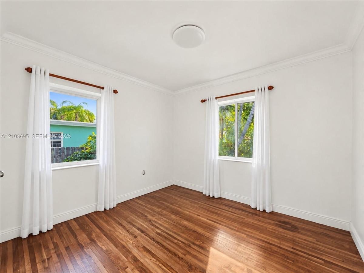 Room featuring wood-finish flooring, dual windows with decorative molding, and crown molding