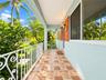 Covered porch featuring multi-tonal ceramic tile flooring, decorative wrought-iron railing, beadboard ceiling, and brick exterior accents
