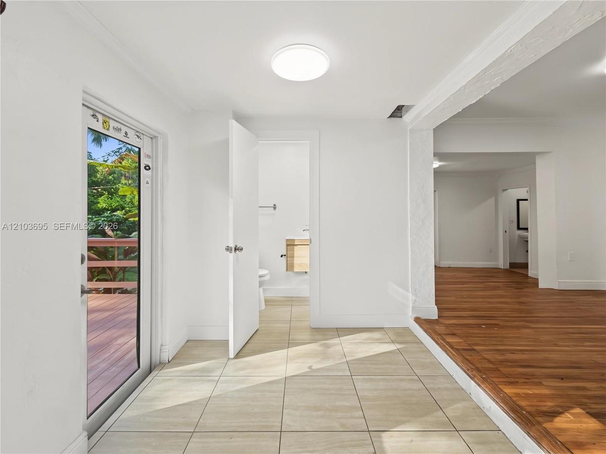 Interior space featuring large-format neutral floor tiling, wood-finish flooring, crown molding, a flush-mount ceiling light fixture, and a glass-pane