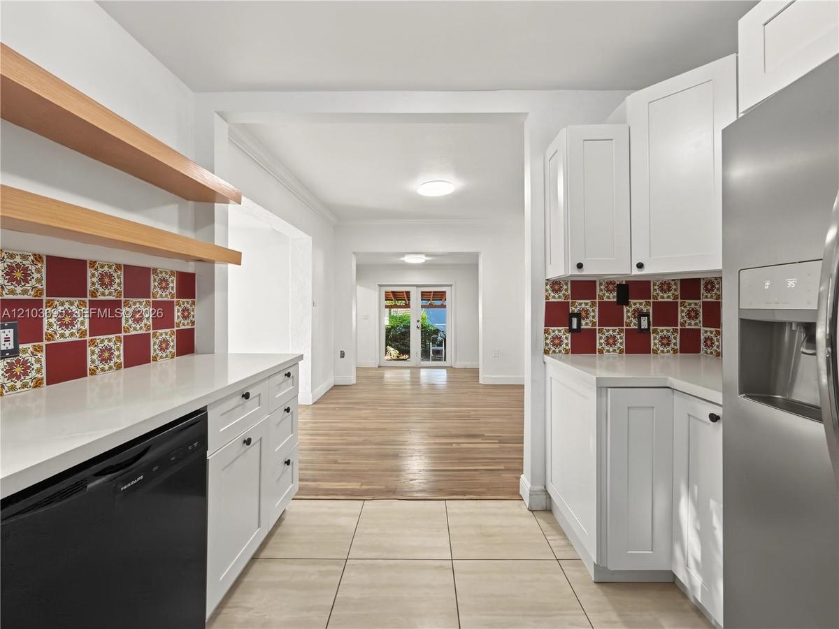 Kitchen featuring white shaker cabinetry, quartz countertops, decorative patterned tile backsplash, natural wood-finish open shelving, and tile floori