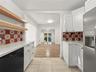 Kitchen featuring white shaker cabinetry, quartz countertops, decorative patterned tile backsplash, natural wood-finish open shelving, and tile floori