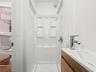 Shower stall with integrated shelving, chrome shower head, wood-finish vanity with a rectangular basin, and single-handle chrome faucet