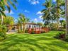 Spacious backyard featuring a wood deck, paved carport, mature palm trees, and extensive landscaping