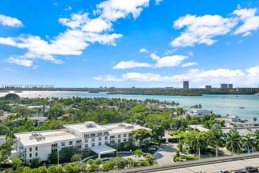 Aerial perspective of coastal property featuring multi-story white building, lush tropical landscaping, paved motor court, and extensive water frontag