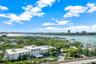 Aerial perspective of coastal property featuring multi-story white building, lush tropical landscaping, paved motor court, and extensive water frontag