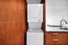 Stacked laundry unit housed within wood-finish cabinetry, featuring stone-surface countertop, flat-panel drawers with horizontal hardware, and a high-