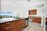 Kitchen featuring wood-finish cabinetry with linear pulls, stone-surfaced countertops, a stainless steel undermount sink with a gooseneck faucet, stai