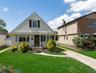 Gable-roof exterior featuring light-toned horizontal siding, arched entryway, multi-pane front windows, and a paved private driveway