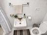 Wall-mounted porcelain sink featuring a metallic dual-handle faucet, surrounded by floor-to-ceiling white ceramic wall tile and chrome-finish bathroom