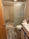 Shower stall featuring a built-in corner bench, sliding frosted glass doors, and wall tile surround, paired with a white vanity featuring a solid surf