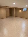 Finished lower-level space featuring tile flooring, vertical wood-panel wall finishing, recessed ceiling lighting, and a structural support column