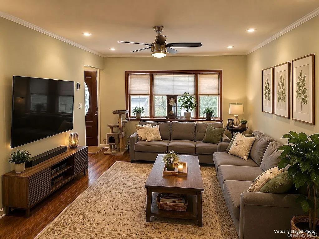 Living area featuring wood-finish flooring, recessed lighting, crown molding, and a multi-panel window configuration with dark wood trim