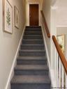 Staircase featuring charcoal carpeted treads, wood handrails, white balusters, and neutral wall tones