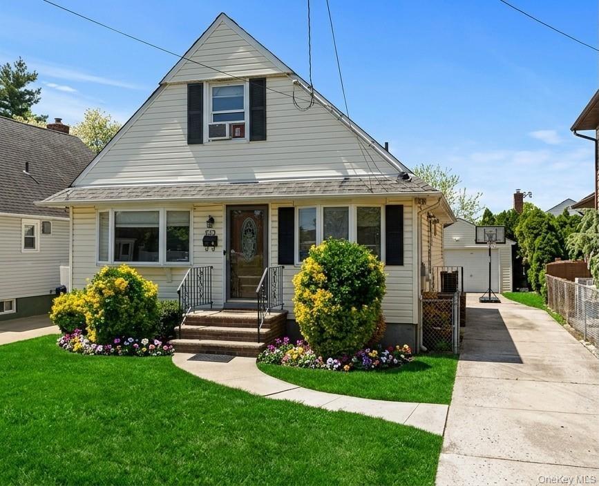 Featuring light-toned vinyl siding, decorative shutters, a concrete driveway, detached garage, and front entryway with stone steps and iron railings