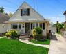 Featuring light-toned vinyl siding, decorative shutters, a concrete driveway, detached garage, and front entryway with stone steps and iron railings