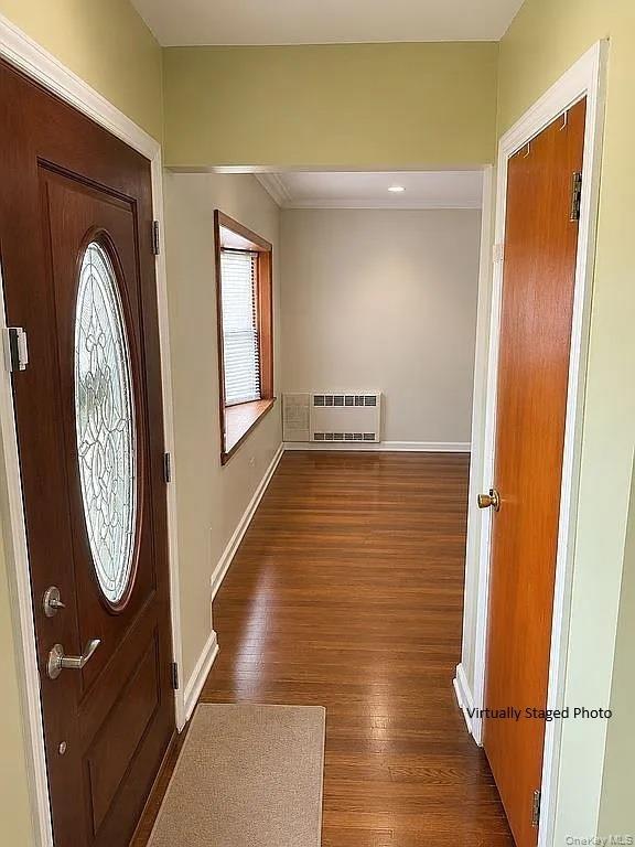 Entryway featuring a solid wood door with oval decorative glass insert, wood-finish flooring, a wood-trimmed bay window, and a built-in wall HVAC unit