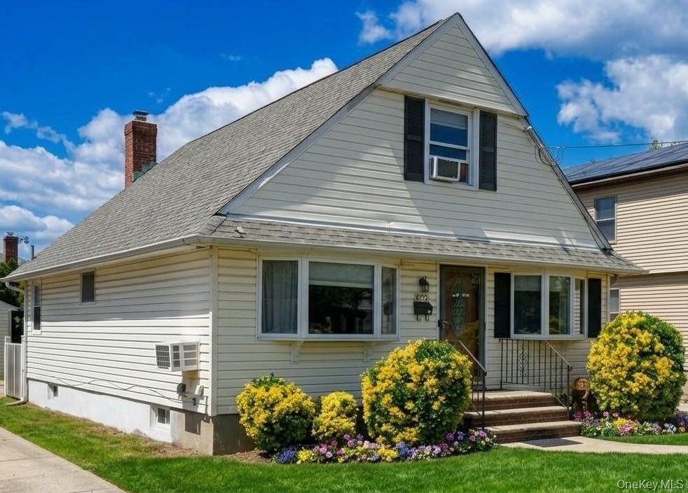 Featuring cream-colored siding, a steeply pitched roof, bay windows, and a brick chimney