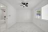 Large-format stone-style tile flooring with veining detail, integrated matte black ceiling fan with light, and wide sliding window