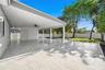 Covered patio featuring ceramic tile flooring, a ceiling fan, white vinyl perimeter fencing, and mature landscaping