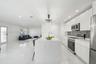 Kitchen featuring white flat-panel cabinetry, a central island with a solid-surface waterfall countertop, stainless steel appliances, a glass-tile bac