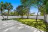Backyard featuring a paved stone patio, mature trees, manicured lawn, and a full-perimeter white vinyl fence