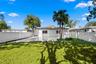 Rear exterior featuring a covered patio, paved hardscaping, white vinyl privacy fencing, and mature palm trees