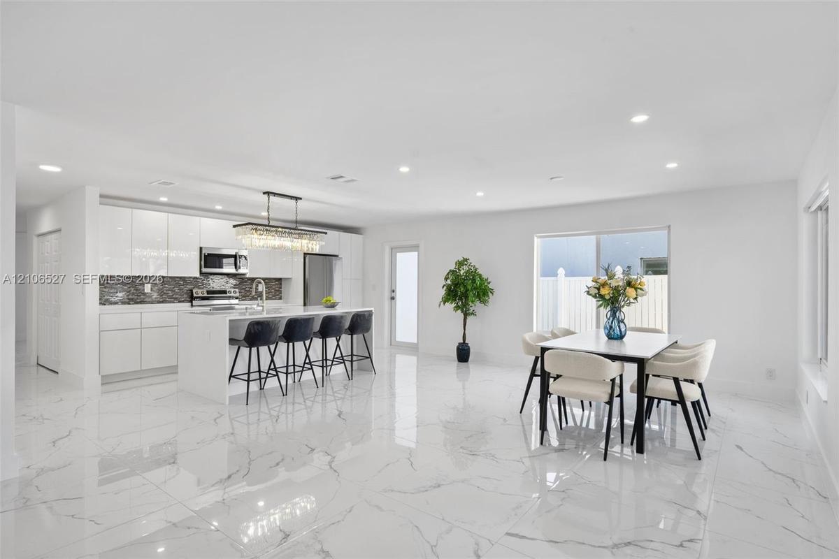 Kitchen featuring white high-gloss cabinetry, stone-finish countertops, stainless steel appliances, a center island with a multi-light pendant fixture
